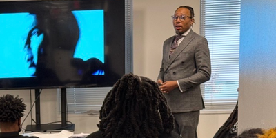 teacher teaching a class while standing by a presentation board