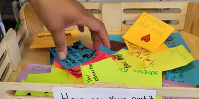 a child's hand reaching into a bin of colorful post-it notes with short messages written on them